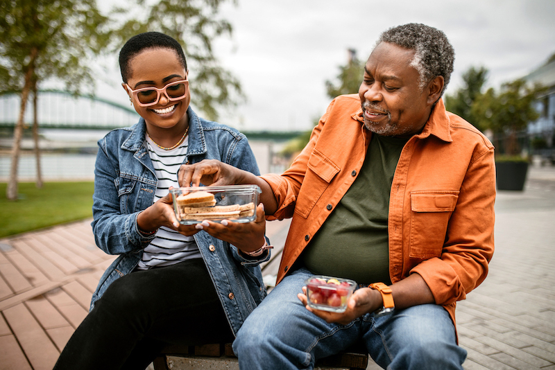 Father and adult daughter sitting outside in an urban park and sharing a picnic lunch.
Due: 5/3