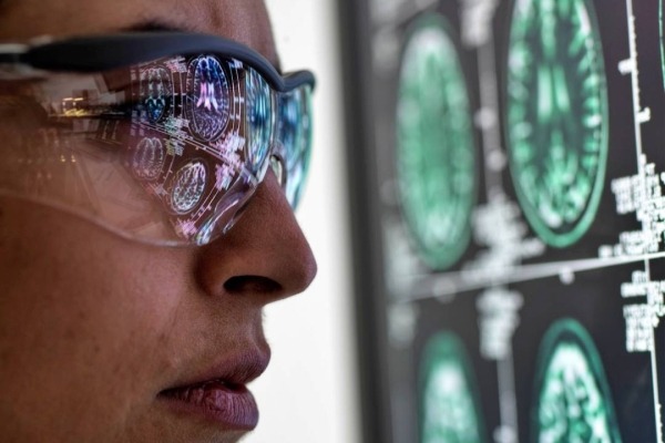 Close of up researcher wearing lab glasses and looking at a human brain scan.